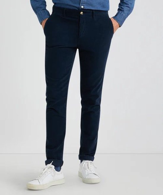Man, staand, voorkant, draagt donkerblauwe chino broek van McGregor met opgerolde broekspijpen.