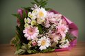 Boeket met roze en witte gerbera's, witte margrieten, roze alstroemeria's en groene varens, verpakt in roze papier.