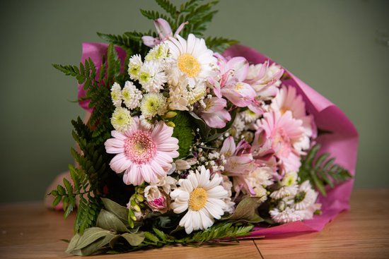 Boeket met roze en witte gerbera's, witte margrieten, roze alstroemeria's en groene varens, verpakt in roze papier.
