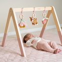 Baby ligt onder houten babygym met speeltjes: bloem, hertje en aardbei.
