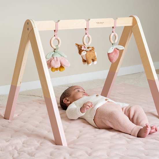 Baby ligt onder houten babygym met speeltjes: bloem, hertje en aardbei.