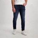 Donkerblauwe, slim fit jeans met lichte slijtage. Een man draagt de jeans met witte sneakers.