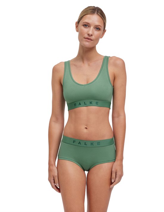 Een vrouw staat in een groene sportbeha en broek met FALKE-band.