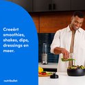 Man met linnen hemd giet groene smoothie in zwarte saladekom naast zilverkleurige Nutribullet blender.