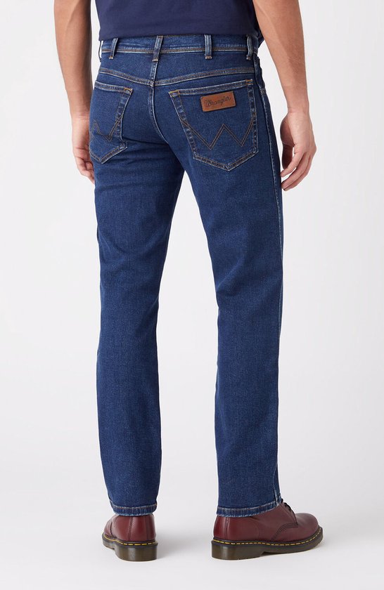 Blauwe Wrangler jeans, regular fit, gedragen met donkerblauw T-shirt en rode schoenen, van achteren gezien.
