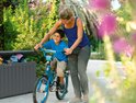 Grijze opbergbox met een open deksel, naast een jongen op een fiets, met een vrouw die helpt.