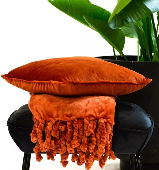Oranje velours kussen op een oranje plaid met gedraaide flosjes, op een zwarte poef.