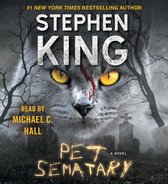 Boekomslag van "Pet Sematary" door Stephen King. Close-up van een grijze kat met gele ogen en bloed op zijn hoofd, met begraafplaats en kale bomen op de achtergrond.