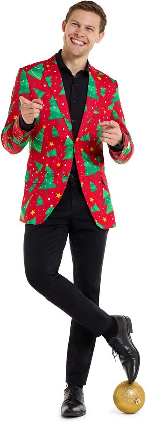 Man met rode kerstblazer met print van groene bomen en sterren, poseert met een gouden kerstbal.