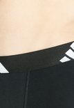 Detail van de zwarte elastische band met witte Adidas logo's op een zwarte boxer.