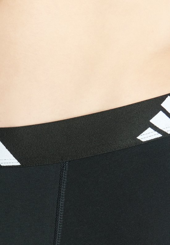 Detail van de zwarte elastische band met witte Adidas logo's op een zwarte boxer.
