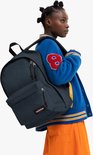 Vrouw met donkerblauwe Eastpak rugzak, blauwe varsity jas met rode '8' en oranje rok.