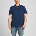 Donkerblauwe polo met rood-wit gestreepte kraag en mouwboorden. Rood logo op borst. Man staat met handen in broekzakken.