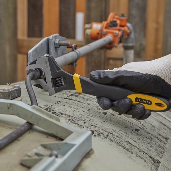 Gloved hand gebruikt Stanley verstelbare moersleutel op gebogen metalen staaf. Zwart en geel handvat.