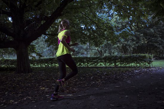 Vrouw in het donker joggend met een fluoriserend geel hesje met roze accenten.