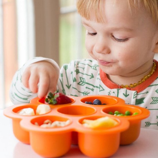 Oranje bloemvormige siliconen bakjes met babyvoeding, gezien vanuit het perspectief van een baby die naar het eten kijkt.