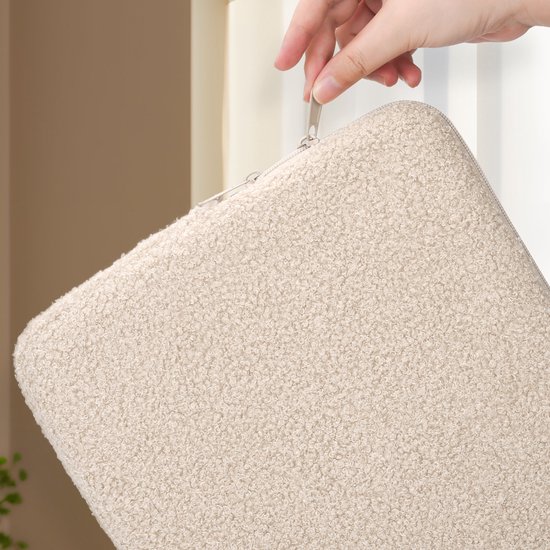 Une main avec une fermeture éclair argentée ouvre une housse d'ordinateur portable en peluche beige.