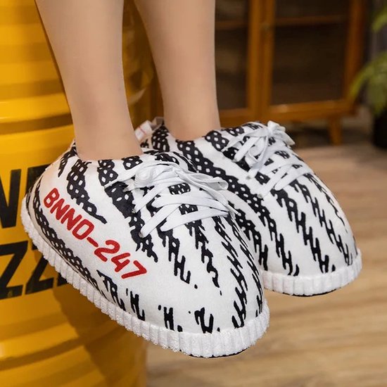Voeten in zwart-witte sneaker-pantoffels bij een gele ton, met rode BNND-247 tekst.