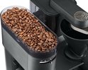 Gedetailleerde close-up van een transparant reservoir gevuld met bruine koffiebonen, bovenop een zwart koffiezetapparaat.