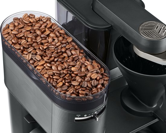 Gedetailleerde close-up van een transparant reservoir gevuld met bruine koffiebonen, bovenop een zwart koffiezetapparaat.