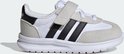 Witte kindersneaker met grijze suède overlays, zwarte Adidas-strepen en klittenbandsluiting.
