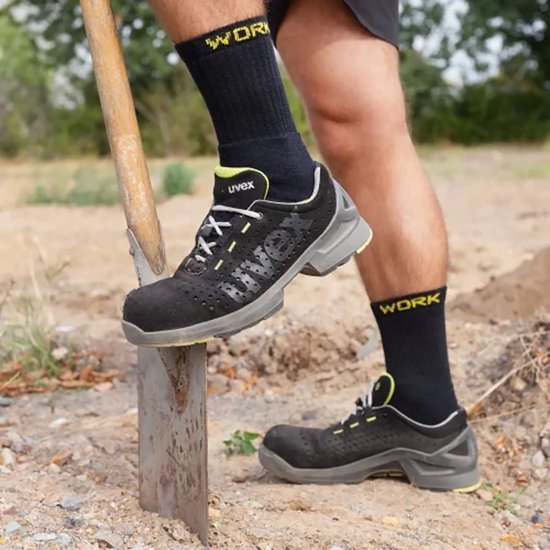 Zwarte werksokken met gele 'WORK' opdruk, gedragen met werkschoenen en een spade.