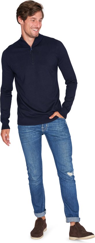 Man met donkerblauwe trui met rits tot de borst, jeans en bruine schoenen.