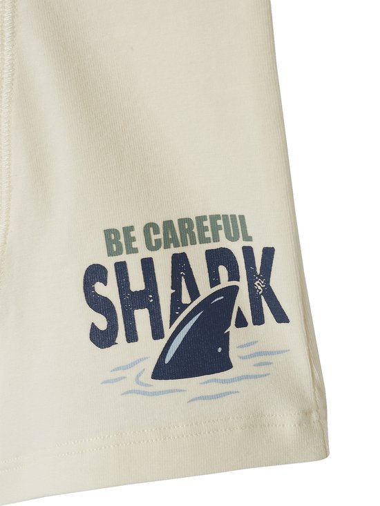 Close-up van crèmekleurige stof met haaienvin print en tekst "BE CAREFUL SHARK".