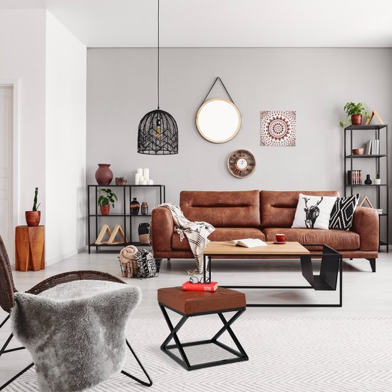 Een bruine leren poef met zwart metalen X-frame staat in een woonkamer voor een bruine bank.