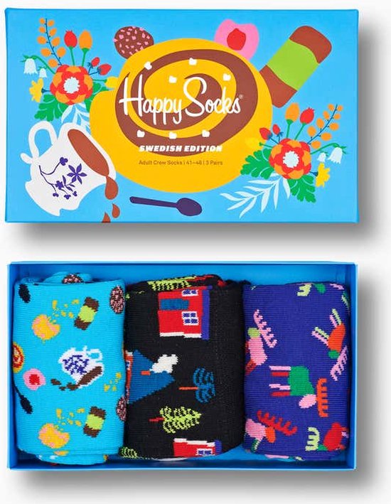 Giftbox met drie Happy Socks in blauw, zwart en paars met patronen van huizen, bomen en abstracte vormen. De verpakking toont een kaneelbroodje.