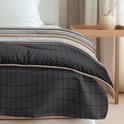 Detail van een dekbed op een bed, met een grafische print van zwarte ruitjes en beige, bruine en grijze strepen.