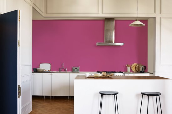Een keuken met fuchsia muur, witte keukenkastjes en kookeiland.