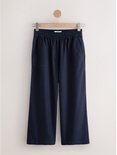 Donkerblauwe wijde broek met elastische tailleband en steekzakken, hangend aan een hanger.