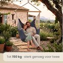 Koppel in een donkerblauwe hangstoel met uitzicht op een tuin bij zonsondergang.