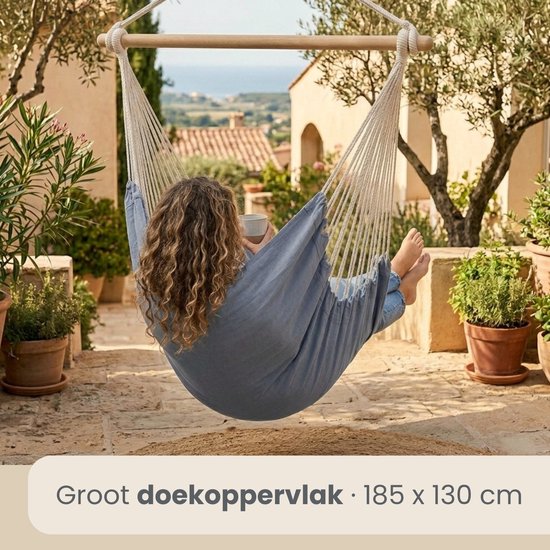 Een vrouw in een blauwgrijze hangstoel op een terras met uitzicht op zee.