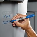 Een hand schrijft met een blauwe Sharpie permanente marker op een grijze opbergbak. Inhoud: TMR 032876.