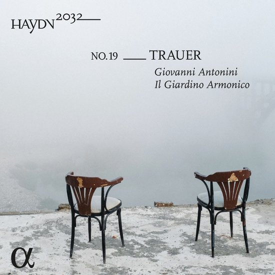Twee lege stoelen op een ruw oppervlak voor een mistige achtergrond. Tekst met "Haydn2032" en "Trauer".