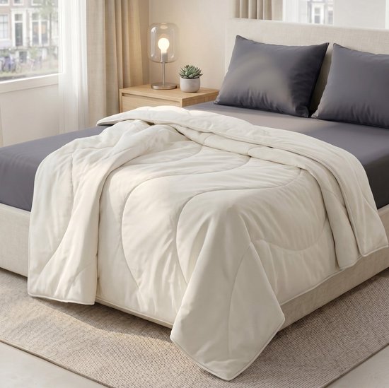 Crème deken met quiltpatroon op een bed met grijs beddengoed, naast nachtkastje.