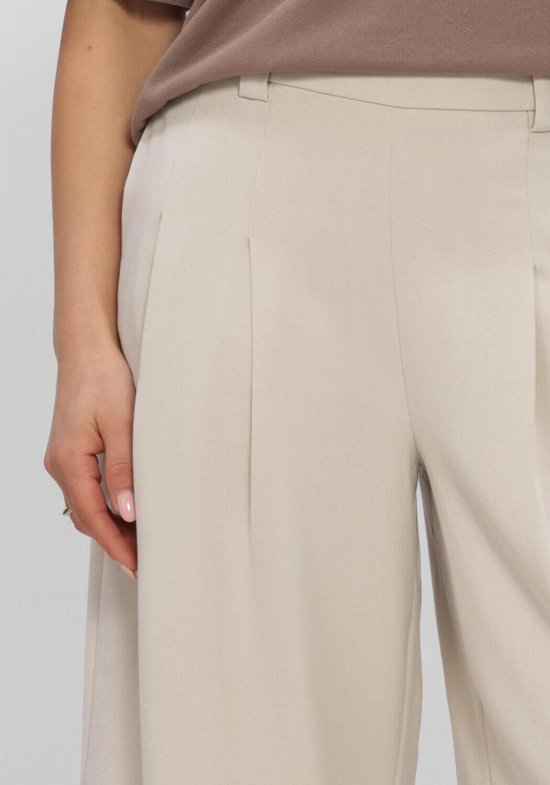 Detail van de plooien aan de zijkant van een beige culotte broek.