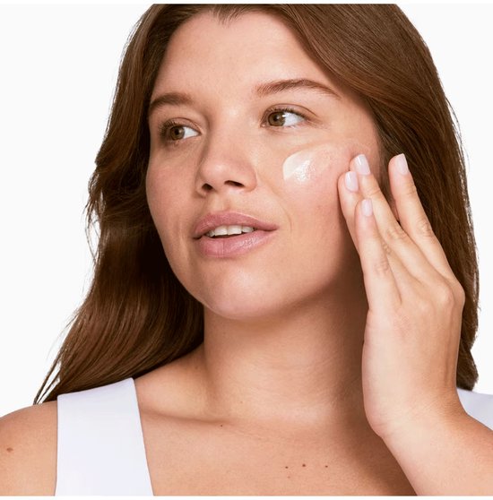 Vrouw met bruin haar brengt een lichte, crèmige lotion aan op haar gezicht.