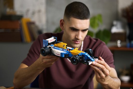 Een man houdt de LEGO Williams FW14B Formule 1 auto vast, met blauwe, gele en witte kleurstelling.