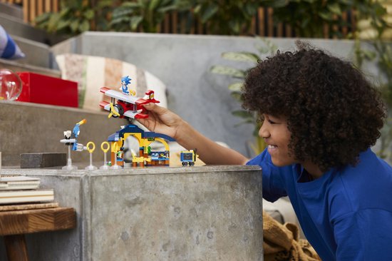 Kind bouwt met de LEGO Sonic Tails' werkplaats-set op een grijze ondergrond.