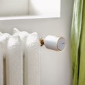 Netatmo slimme thermostaatknop, zilverkleurig met oranje accent, op een crèmekleurige gietijzeren radiator.
