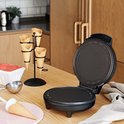 Open zwart wafelijzer op een houten aanrecht met wafelhoorntjes, schepje en ijshoornvorm.