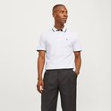 Model draagt wit poloshirt met zwarte biezen, zwart logo en zwarte broek.