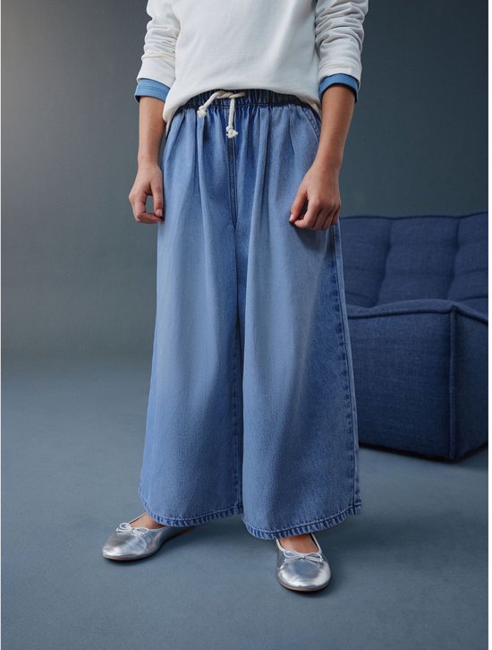 Kind draagt wijde, ronde jeans in lichtblauw denim, met strikdetail aan de tailleband.