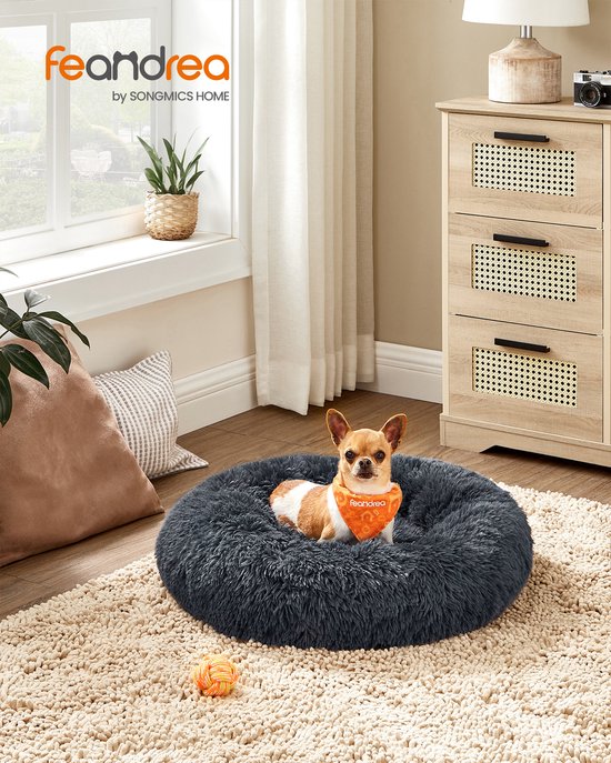 Een klein hondje met oranje bandana in een donkergrijs pluizig bed in een woonkamer.