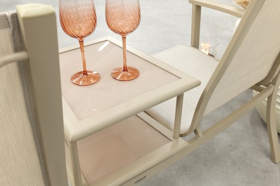 Close-up van een beige aluminium tuinbank met stoffen zitting en een glazen tafelblad.