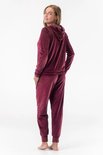 Model draagt een bordeauxrode velours loungewear set. De set bestaat uit een hoodie met rits en zakken, en een joggingbroek.