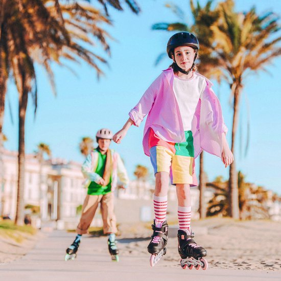 Meisje met zwarte helm en roze gestreepte blouse rolschaatst, omringd door palmbomen.